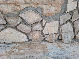 Fototapeta premium Building a rustic stone wall using beige limestone and grey cement mortar in a construction site