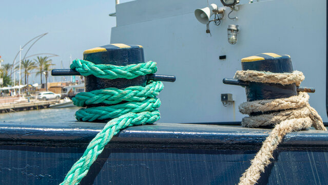 Bright green synthetic and classic hemp mooring ropes tied around metal bitts on a commercial vessel at a port during daytime