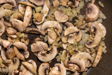 Fototapeta premium Macro close-up of sliced mushrooms and diced onions sautéing together in a hot skillet pan