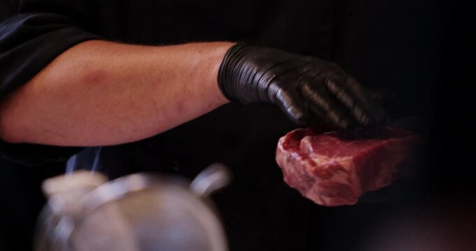 A chef wearing black gloves points at and inspects a raw marbled beef steak piece