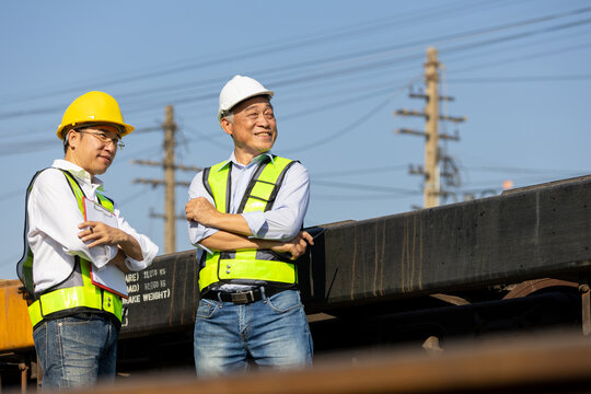 Engineers in safety gear standing and talking at railway freight terminal, Logistics team inspecting operations at cargo railway station, Industrial manager in hardhat and safety vests at railway site