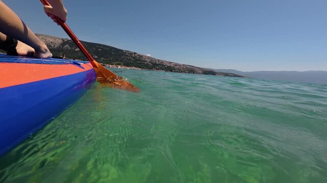 Close-up POV video of a paddle blade cutting through the crystal clear Adriatic Sea while stand up paddleboarding near Ba&scaron;ka on Krk Island, Croatia. vibrant summer atmosphere