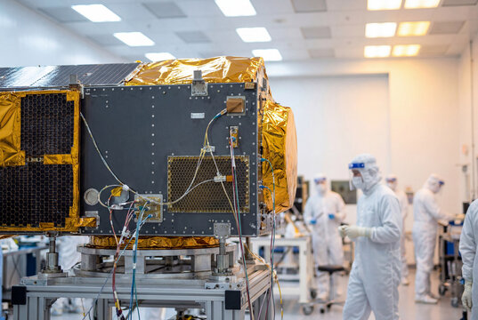 Satellite testing inside cleanroom with engineers operating spacecraft systems