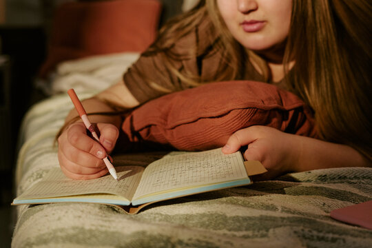 Plus size girl writing in journal while lying on bed, reflecting on thoughts and daily routine. Suitable for mental health, self care, youth wellbeing, or diary app marketing