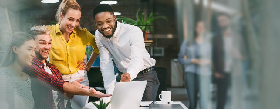 Smiling Black Man Working With Three Colleagues In Office Environment, Discussing Ideas And Collaborating On Project In Creative Workspace. Group Of Young Professionals Engaged In Work.