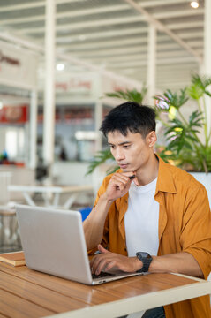 Asian man focused on surfing the internet with laptop while sitting at table in a contemporary cafe.