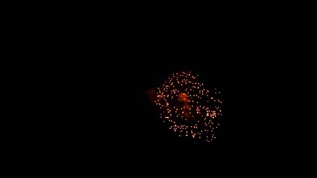 Colorful fireworks exploding and sparkling in the dark night sky during holiday celebration, captured in real time wide shot.