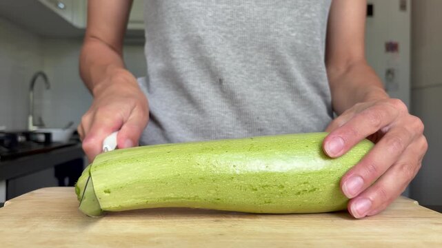 Woman slicing fresh green zucchini on a wooden cutting board in kitchen. A moment of healthy food preparation.