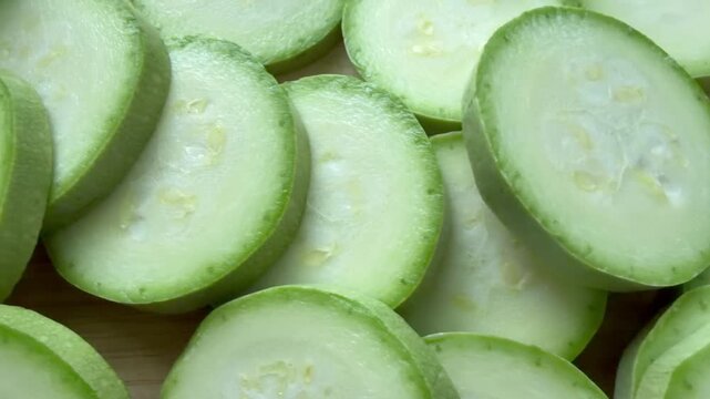 fresh, raw zucchini slices arranged on a light wooden cutting board.