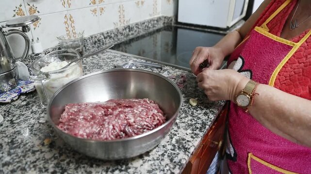 Mujer mayor agregando carne molida y ajo en un taz&oacute;n para mezclar. Abuela mayor mezclando carne molida y ajo en un taz&oacute;n. Receta tradicional de alb&oacute;ndigas caseras, aut&eacute;ntica cocina senior.