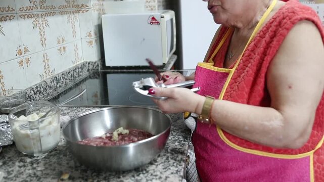  Mujer mayor agregando carne molida y ajo en un taz&oacute;n para mezclar. Abuela mayor mezclando carne molida y ajo en un taz&oacute;n. Receta tradicional de alb&oacute;ndigas caseras, aut&eacute;ntica cocina senior.