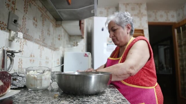  Mujer mayor agregando carne molida y ajo en un taz&oacute;n para mezclar. Abuela mayor mezclando carne molida y ajo en un taz&oacute;n. Receta tradicional de alb&oacute;ndigas caseras, aut&eacute;ntica cocina senior.