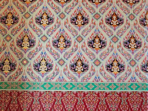 A detailed wall painting or wallpaper featuring traditional Thai patterns, with repeating motifs of celestial beings (Devas) with hands in a praying gesture (Wai), accented by green and red decorative