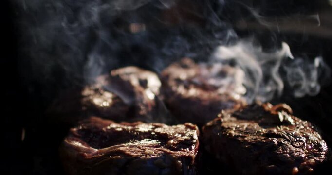 Close up view of hand using tongs to turn juicy meat steaks on hot smoky barbecue grill grate