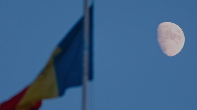 Sharp Gibbous Moon in the Twilight Sky Beside a Blurred Moldovan Flag