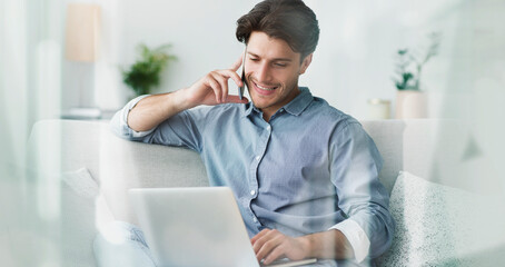 Fototapeta premium Smiling Young Caucasian Man Engaged In Conversation On Mobile Phone While Working On Laptop At Cozy Home Office. Focused And Happy Individual Utilizing Technology In A Modern Setting.