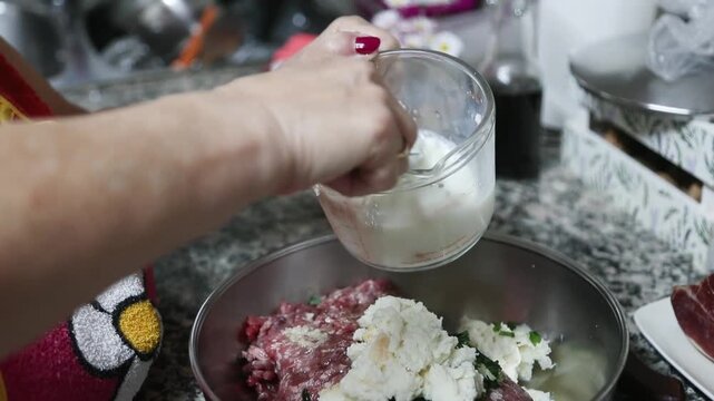 Mujer mayor agrega pan empapado en leche al taz&oacute;n para mezclar alb&oacute;ndigas. Abuela mayor agrega pan empapado en leche al taz&oacute;n. Receta tradicional de alb&oacute;ndigas caseras, aut&eacute;ntica cocina senior.