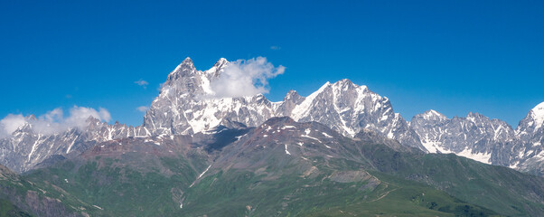 Fototapeta premium Georgia Caucasus panoramic snow capped mountain range under blue sky, alpine landscape, adventure travel, hiking destination.