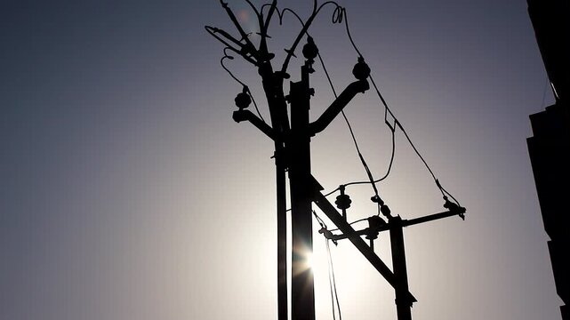 Dramatic silhouette of utility pole and overhead power lines against bright sky. Ideal for electricity, energy infrastructure, power supply, grid and utility industry projects.