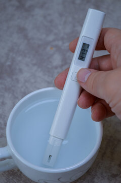 Digital TDS water tester held in a hand, measuring the purity of liquid in a white cup. Ideal for health, water quality, filtration, household testing, and scientific content.