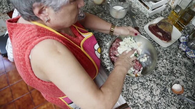  Mujer mayor mezclando ingredientes de alb&oacute;ndigas a mano en un taz&oacute;n. Abuela mayor amasando y mezclando ingredientes de alb&oacute;ndigas a mano en un taz&oacute;n. Cocina tradicional casera, aut&eacute;ntica senior.