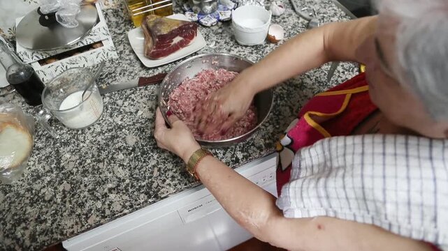  Mujer mayor mezclando ingredientes de alb&oacute;ndigas a mano en un taz&oacute;n. Abuela mayor amasando y mezclando ingredientes de alb&oacute;ndigas a mano en un taz&oacute;n. Cocina tradicional casera, aut&eacute;ntica senior.
