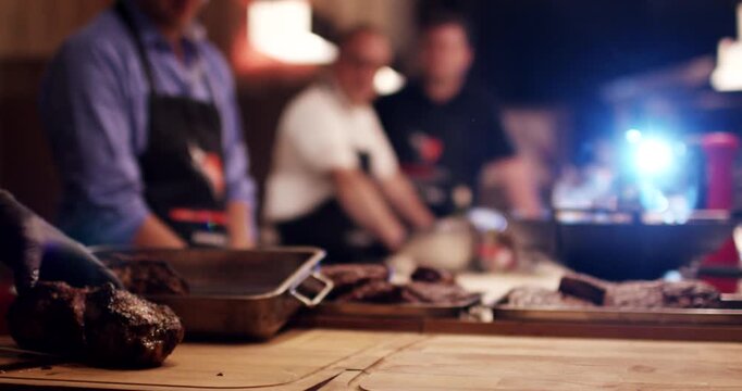 Selected focus on dark roasted meat on table with people in background at cooking workshop