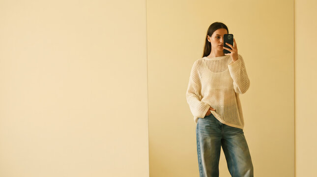 Young woman taking a mirror selfie in a minimalist bright room
