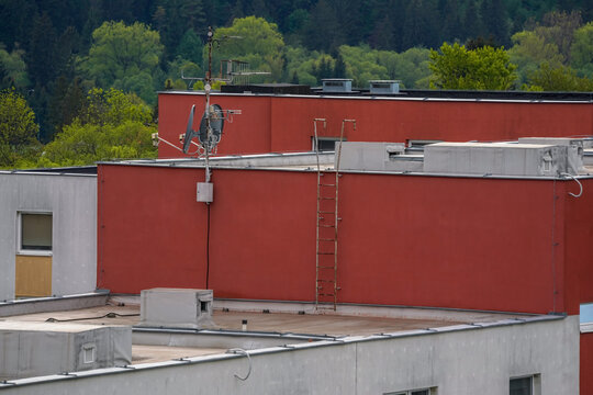 Roof of flats apartment building, satellite dishes, and ladder to raised level, closeup detail, blurred trees background
