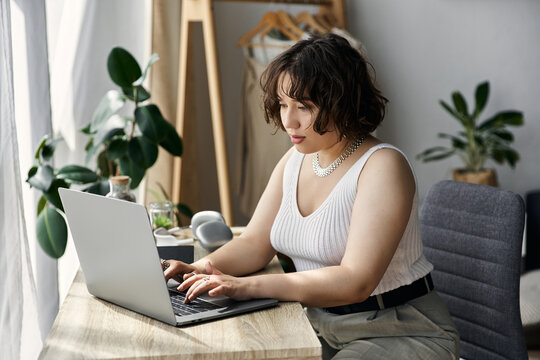 Young woman focuses on her laptop while sitting in her modern, bright apartment.