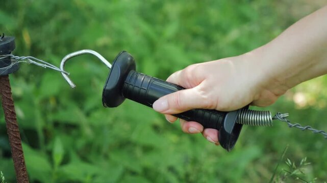 Close-up of a hand opening an electric fence handle attached to a wire barrier in a rural forest area. Agricultural fencing system used to control livestock movement and provide access along