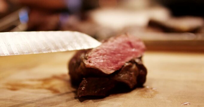 Close up view of freshly cut piece of medium rare steak on wooden cutting board with knife