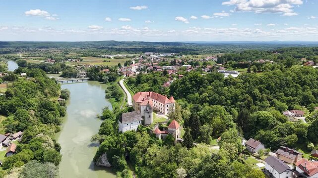 Aerial view of the historic Ozalj Castle perched on a cliff above the Kupa River, surrounded by lush green forests and the town of Ozalj, Karlovacka zupanija, Croatia.