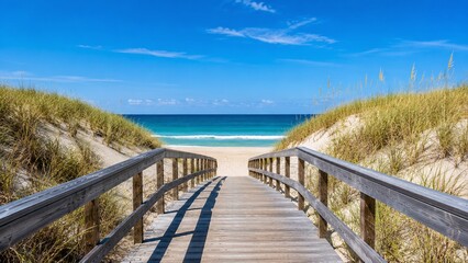 Obraz premium Wooden boardwalk through coastal sand dunes leading to turquoise beach and blue sky