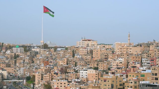 Large Jordan flag waving above many buildings in central Amman, group of birds flaying near
