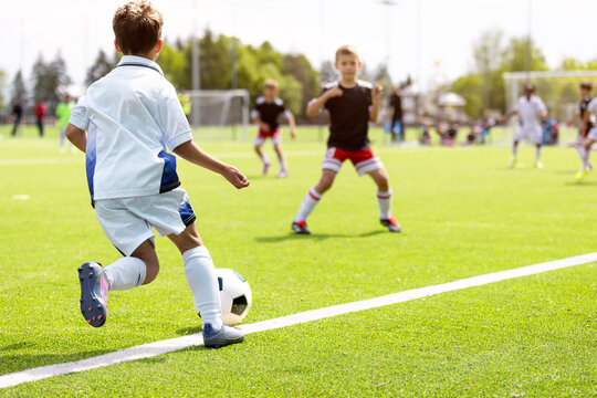 Young Football Player Dribbling: Youth Soccer Action Shot from Back View on Grass Field
