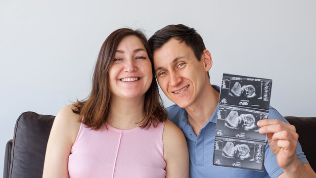 Happy smiling and holding a sonogram printout, announcing their pregnancy and preparing for parenthood in a moment of celebration and future planning