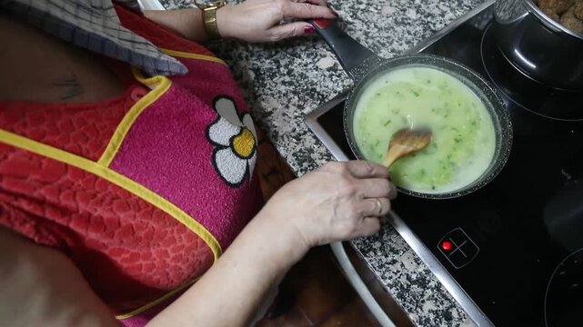  Mujer mayor preparando salsa con caldo, harina y aceite. Abuela mayor preparando salsa tradicional con caldo, harina y aceite en cacerola. Aut&eacute;ntica cocina casera.