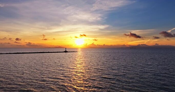 Golden sunrise over the sea with the silhouette of a lighthouse and breakwater in Zhuhai, China