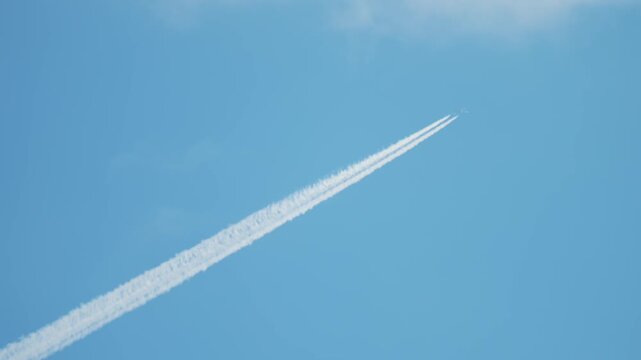 Airliner flying high leaving long white contrail across blue sky, aviation route and flight path concept. Jet exhaust plume forming chemtrail pattern linked with air pollution and climate change