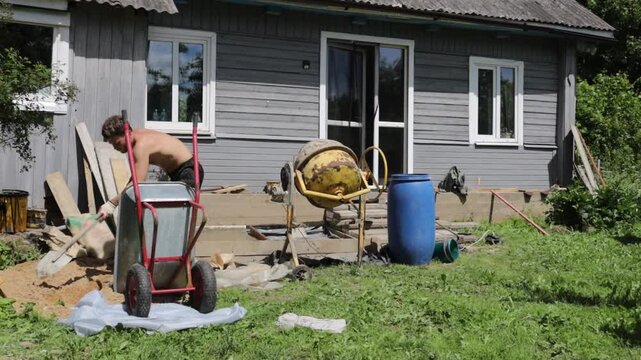 A man mixes concrete mortar for house repairs and foundation replacement, using a concrete mixer