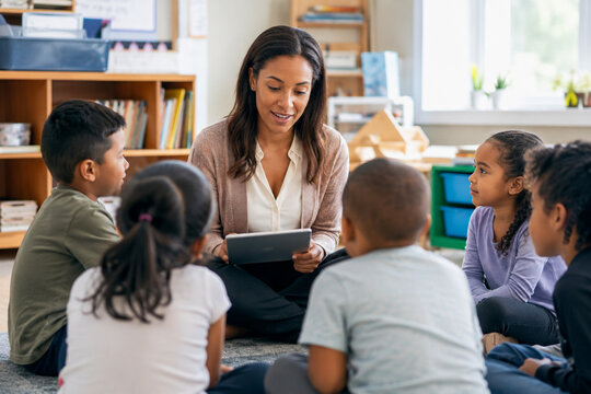 A friendly female teacher reading a story to a group of diverse young children in a classroom.