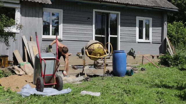 A man mixes concrete mortar for house repairs and foundation replacement, using a concrete mixer