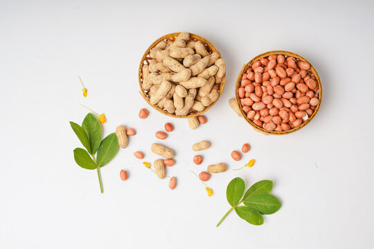 Two baskets of peanuts, one with shells and one without, arranged with scattered nuts and green leaves