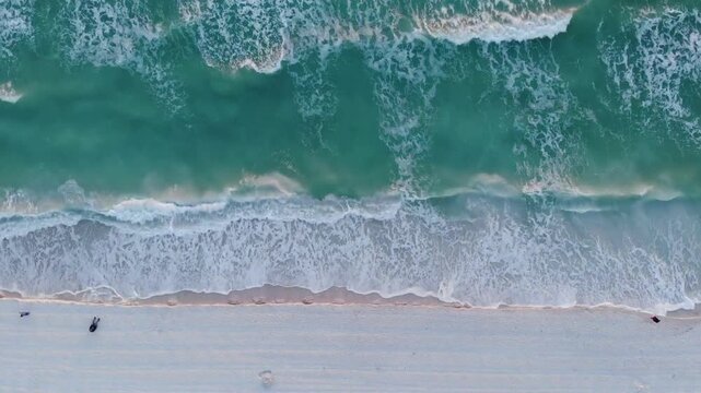Aerial top down view of turquoise ocean waves crashing on white sand beach. Cinematic drone shot of tropical sea shoreline and emerald water ripples.
