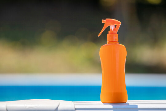 Vibrant orange sunscreen spray bottle beside a blue swimming pool, evoking summer protection, vacation relaxation, and healthy outdoor lifestyle