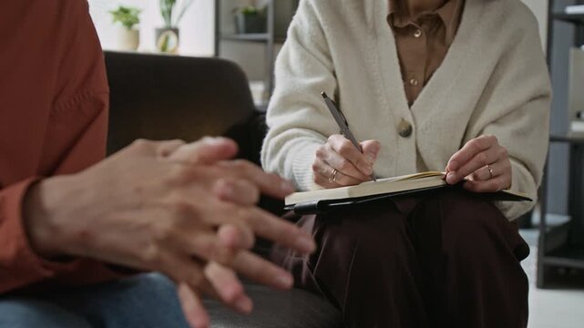 Close up of middle aged patient wringing hands during therapy session while female psychotherapist takes notes. Clip is ideal for mental health services and psychological counseling commercials