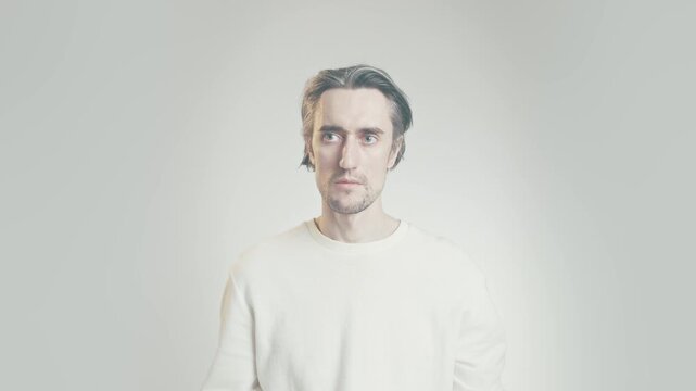 Young adult man with short tousled hair in light ribbed sweater, neutral expression, close up studio portrait on bright gradient background