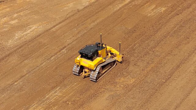 Powerful bulldozer pushing soil and leveling construction ground with steel blade. Aerial earthmoving operations highlighting heavy equipment, land grading workflow, infrastructure site preparation