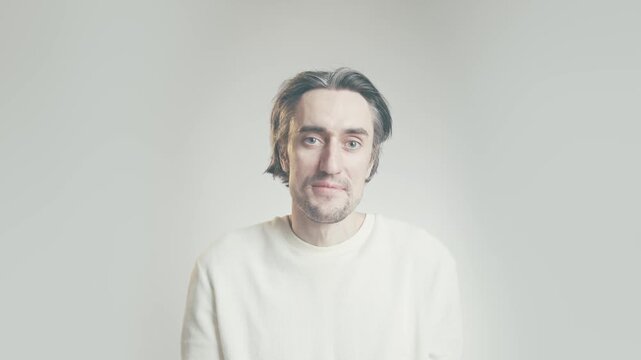 Middle aged man extending hand for handshake, white sweater, soft daylight portrait on minimalist gray background with copy space